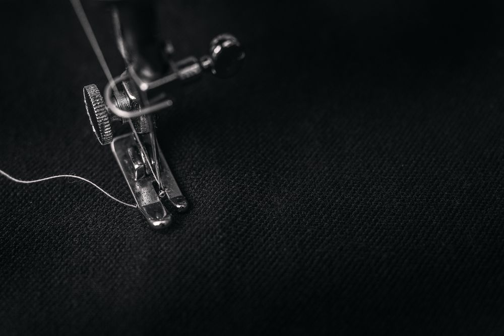 A sewing machine needle and thread on dark cloth